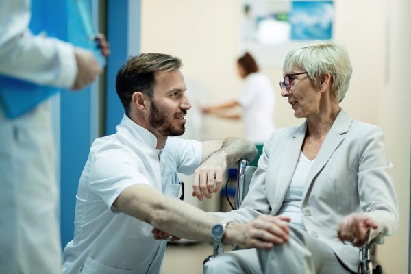 Senior woman in wheelchair and mid adult doctor talking in a hallway in the hospital.